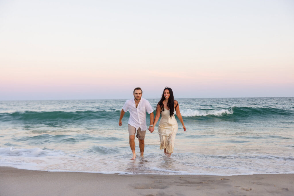 Catie and Zach run through the waves together during their Fire Island National Seashore engagement session at sunset.