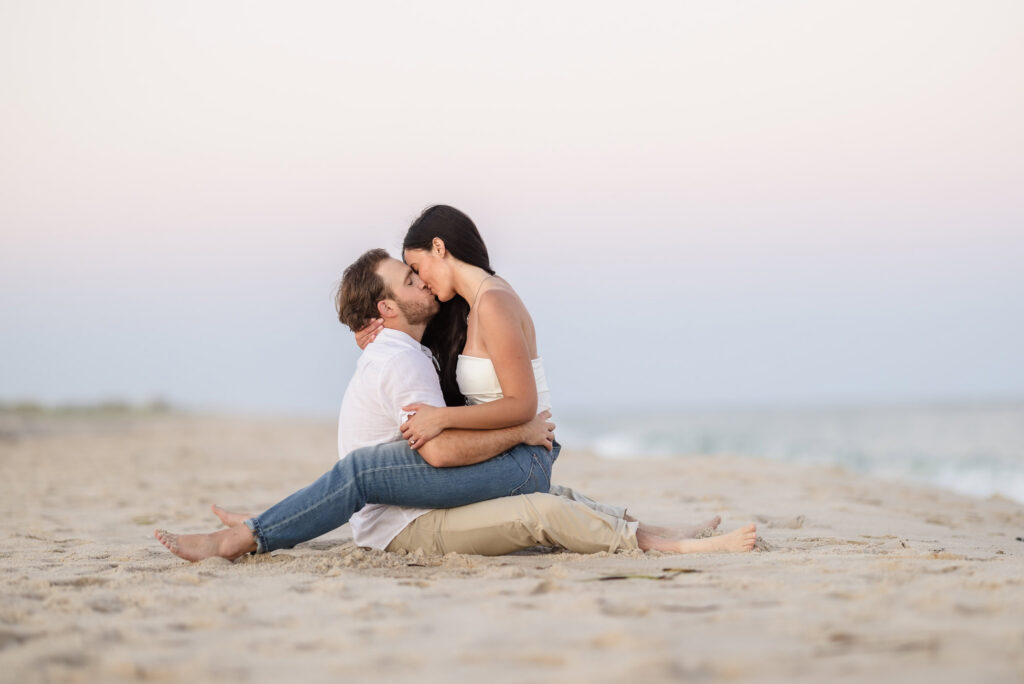 Catie and Zach share a quiet kiss while sitting together on the sand during their casual engagement session at Fire Island National Seashore.