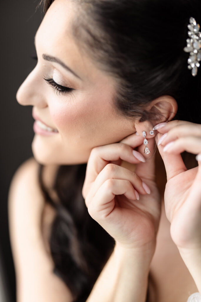 Bride fastening her diamond drop earrings while getting ready for her Harbor Club at Prime wedding.