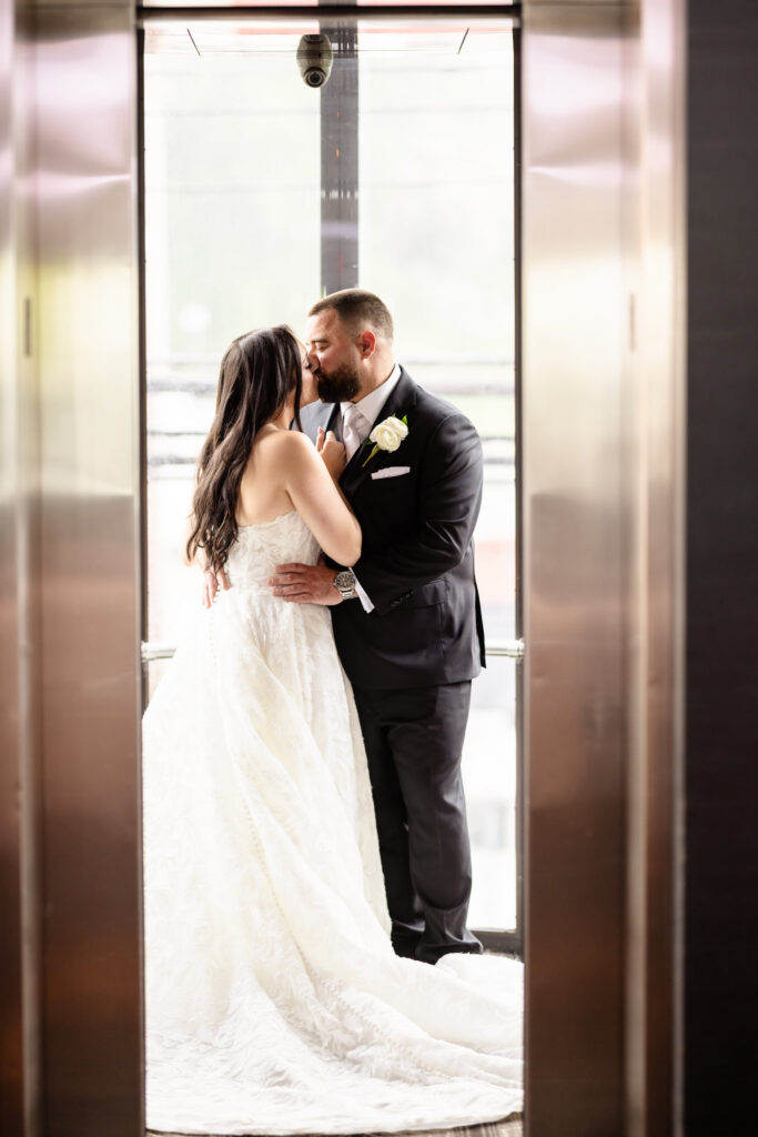 Bride and groom sharing a kiss inside the glass elevator during portraits for their Harbor Club at Prime wedding.