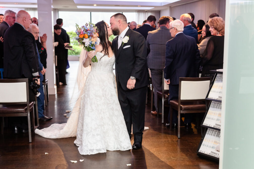 Newlyweds share a kiss while walking back down the aisle after their Harbor Club at Prime wedding ceremony surrounded by family and friends.