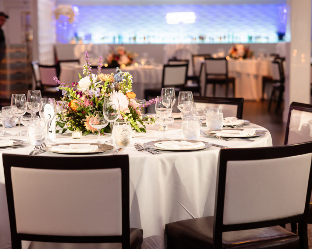 Reception table decorated with colorful floral centerpiece and elegant place settings.