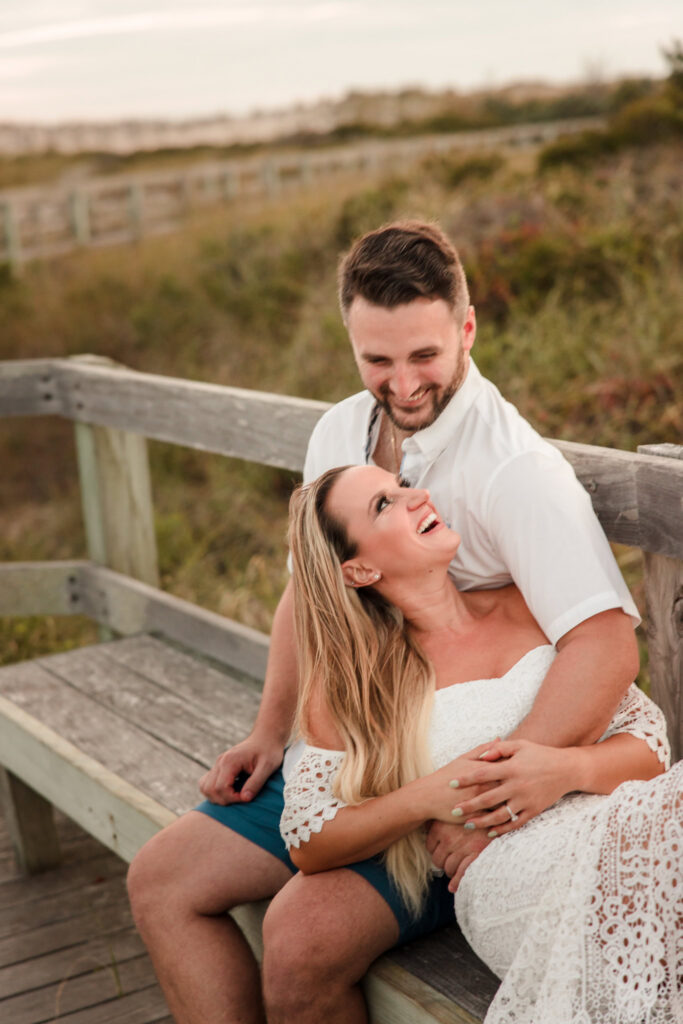 Laughing couple seated together on the boardwalk during a relaxed Fire Island engagement session.