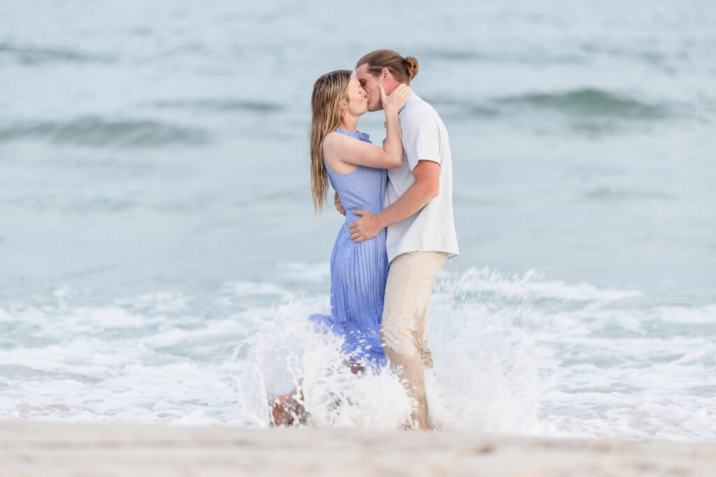 Couple kissing in the surf as waves break around them during a Fire Island beach engagement session.