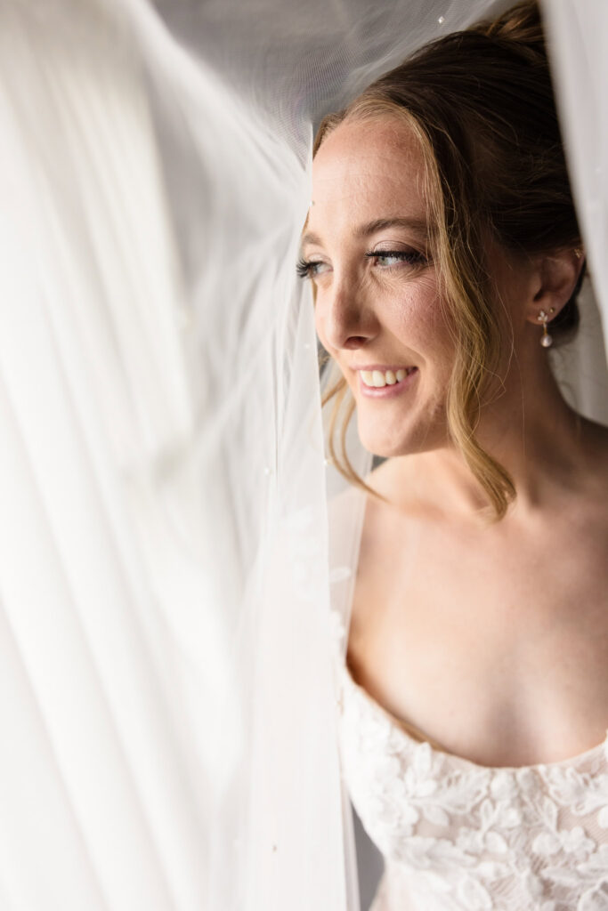 Close-up portrait of Lauren smiling beneath her wedding veil in soft natural window light.