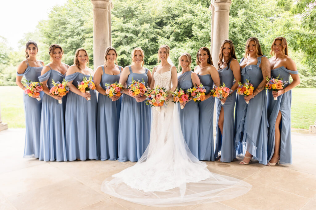 Bride Lauren posing with her bridesmaids beneath the covered arches at Planting Fields Arboretum before her Watermill Caterers wedding reception.