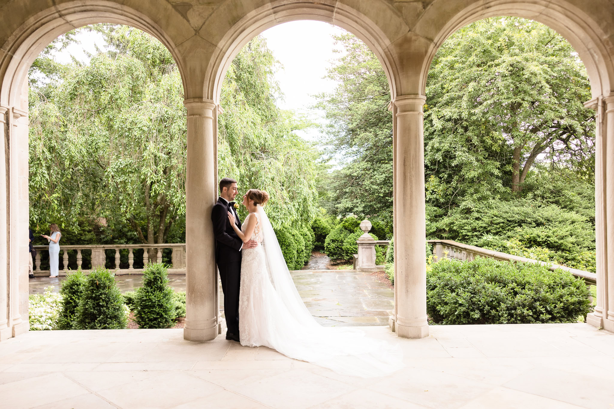 Lauren and Joe sharing a quiet portrait beneath the covered arches at Planting Fields Arboretum during light rain.