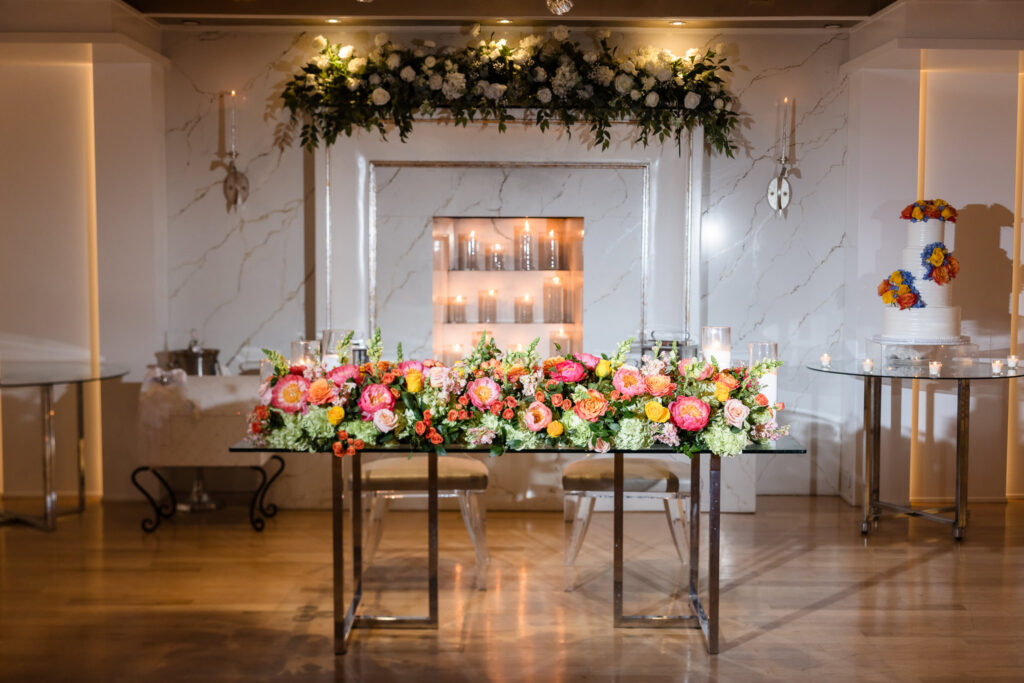 Elegant sweetheart table with colorful floral arrangements, candles, and fireplace backdrop at Watermill Caterers.