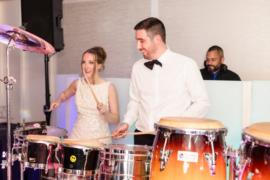 Bride and groom playing percussion instruments alongside the DJ during the reception celebration at Watermill Caterers.