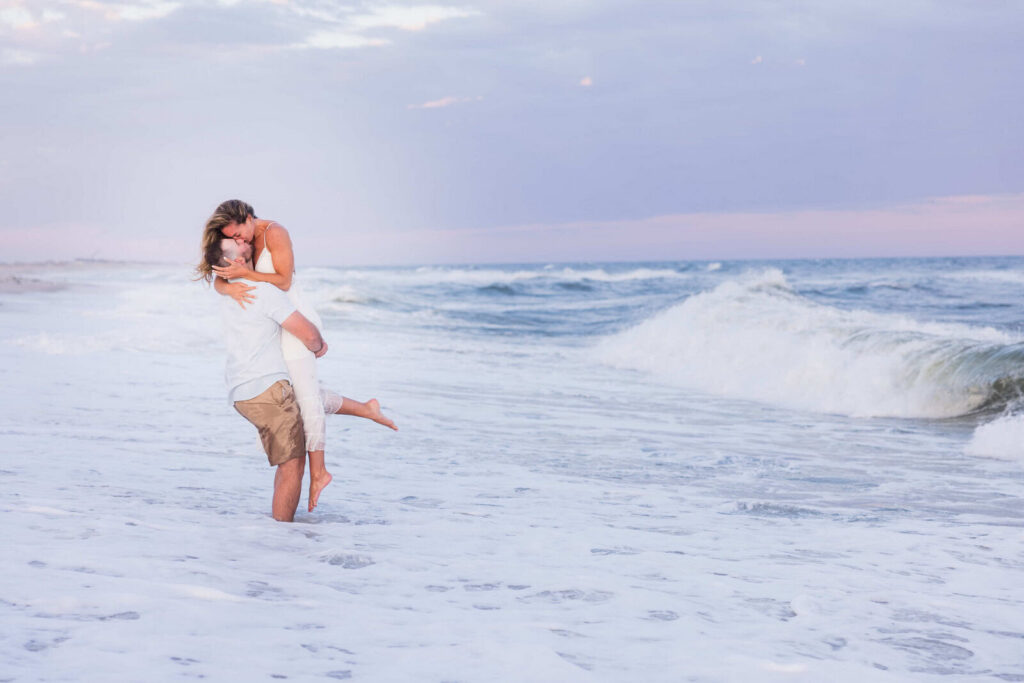 Engaged couple embracing in the ocean during a romantic Long Island beach engagement session.