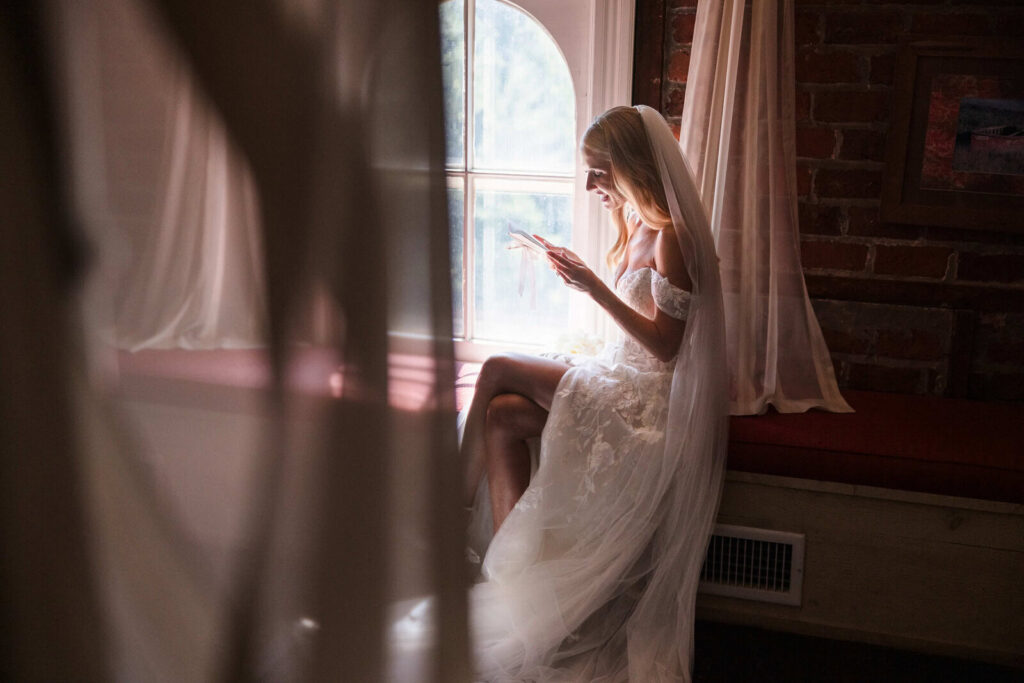 Bride sitting beside a window reading a letter during a quiet, emotional moment before her wedding ceremony.