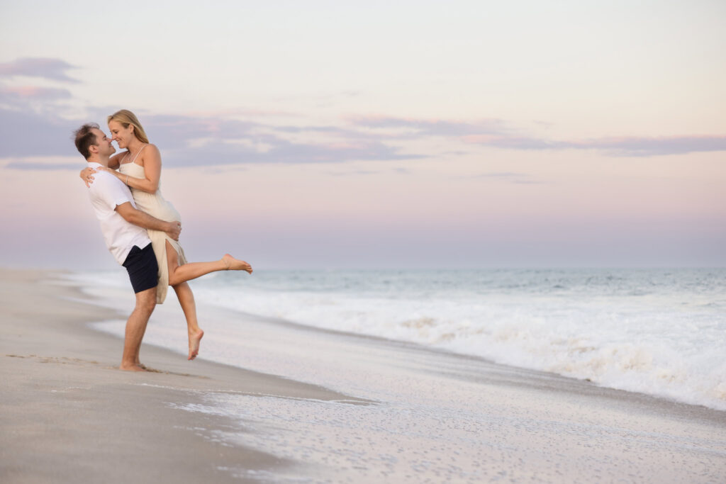 Couple sharing a playful moment along the Fire Island shoreline as soft evening light settles over the ocean.