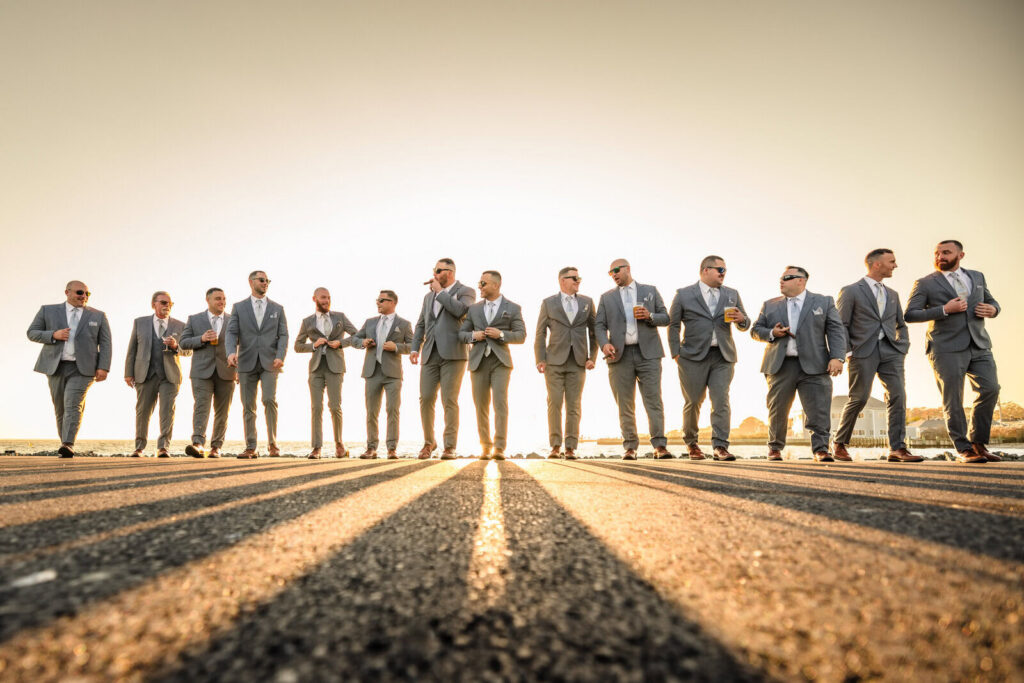Groomsmen in matching gray suits walking together in warm golden-hour light near the waterfront.