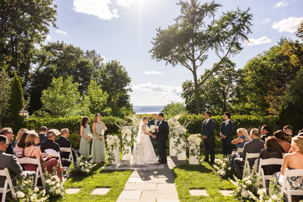 Bride and groom exchanging vows during an elegant outdoor garden wedding ceremony surrounded by white flowers and guests.