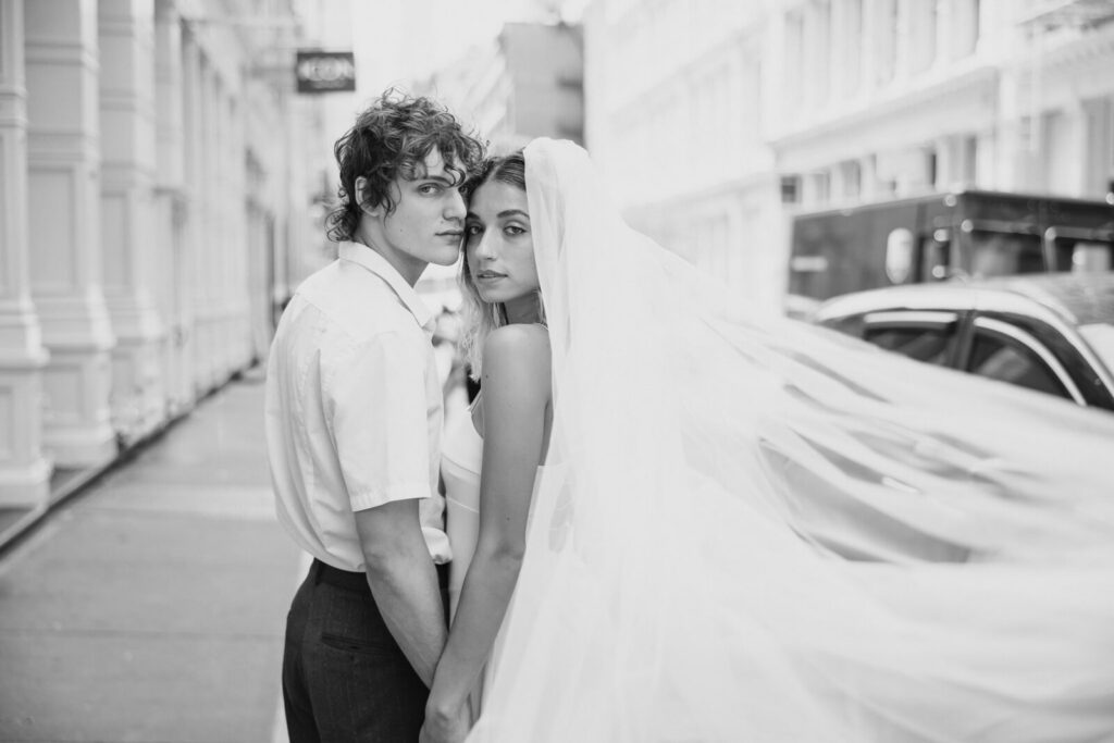 Black-and-white portrait of a wedding couple on a New York City street with the bride’s veil flowing behind them showing how much their Long Island wedding cost.