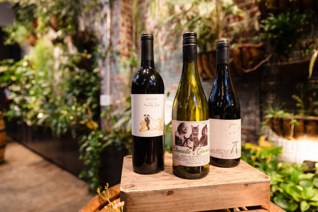 Three wine bottles with personalized labels displayed against the living plant wall.