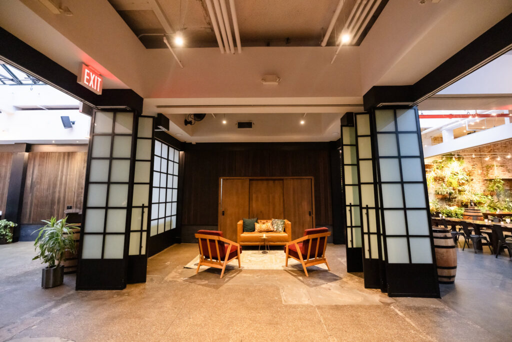 Modern lounge area at Brooklyn Winery with black-framed doors, leather seating, and views toward the living plant wall.