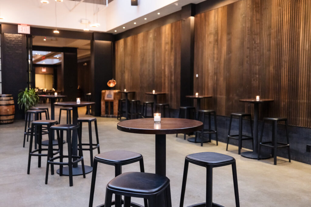 Cocktail hour space at Brooklyn Winery with high-top tables, black stools, wood-paneled walls, and candlelight.