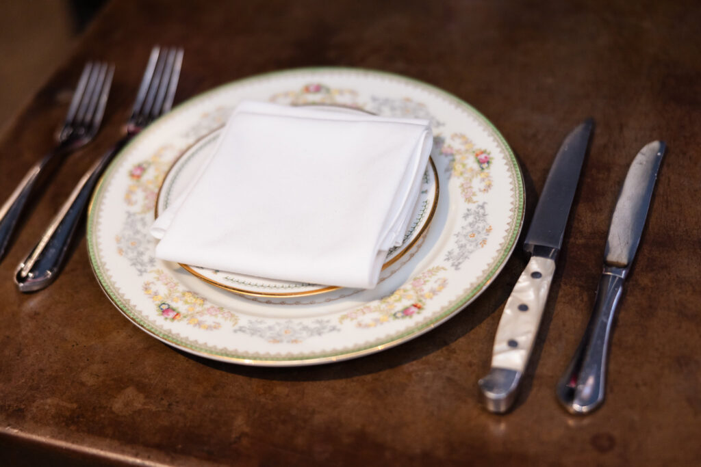 Vintage floral china, white linen napkin, and silverware arranged on a wooden table.