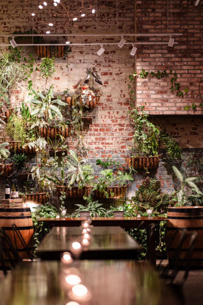 Vertical view of Brooklyn Winery's signature living plant wall with exposed brick, greenery, wine barrels, and candlelit tables.