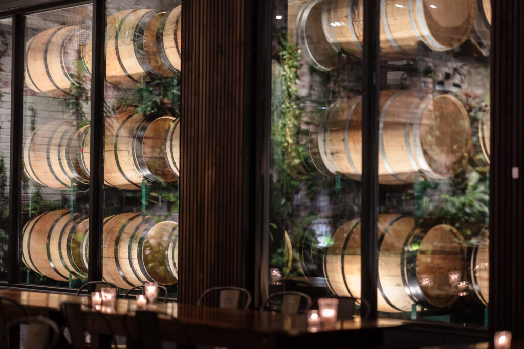 Rows of wooden wine barrels visible behind glass beside candlelit tables.