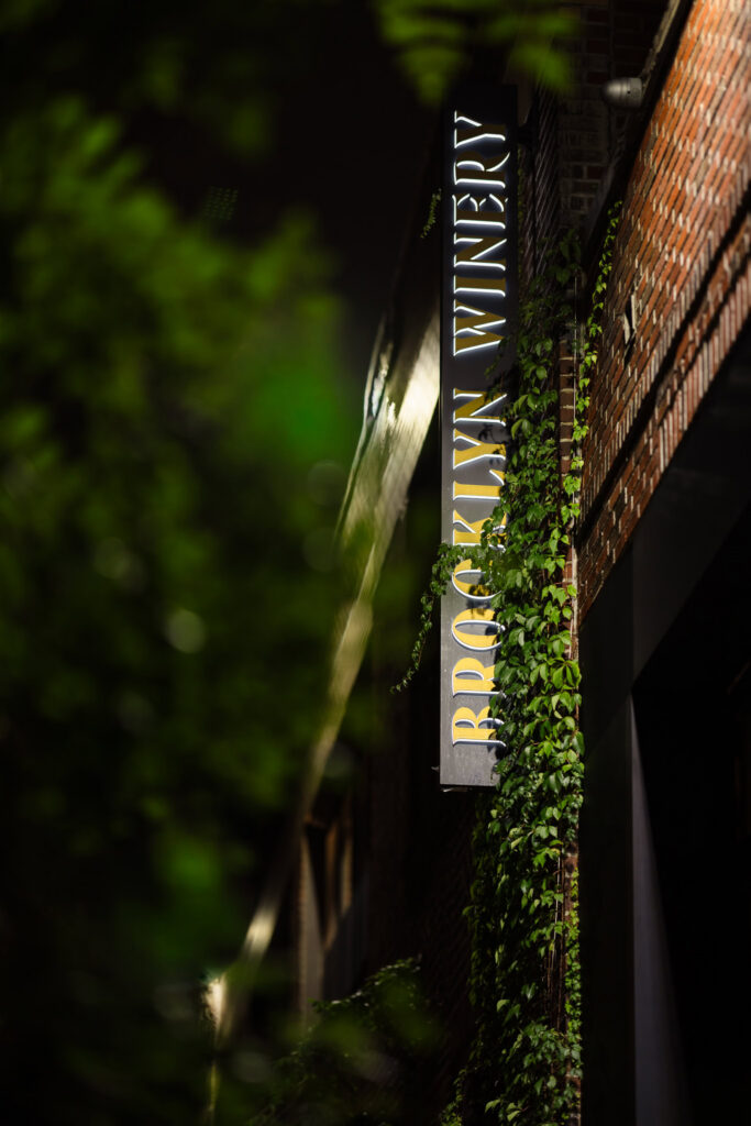 Illuminated Brooklyn Winery sign surrounded by ivy outside the venue on Guernsey Street in Williamsburg.