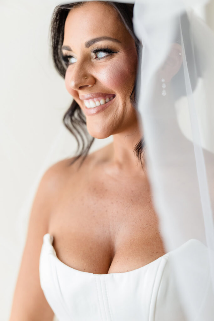 Close-up bridal portrait of Christine smiling beside her veil before her Muttontown Club wedding ceremony.