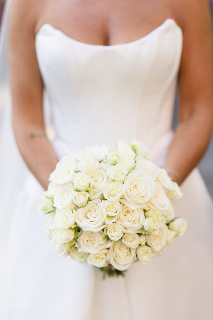 Close-up of Christine's classic white rose bridal bouquet against her wedding gown at The Muttontown Club.