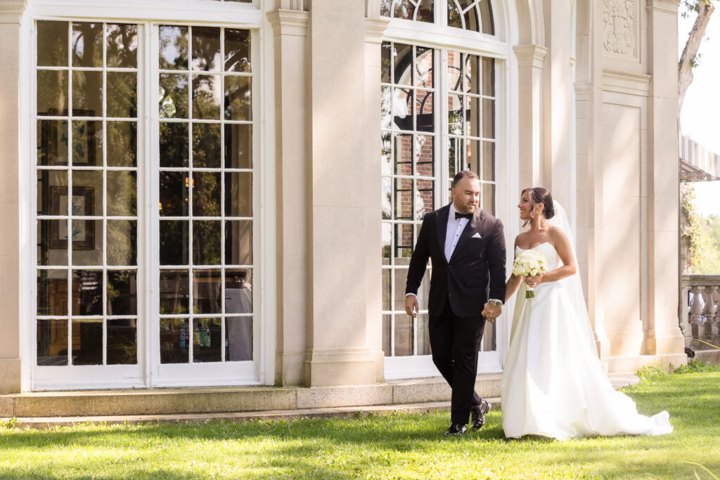 Bride and groom walking hand in hand outside The Muttontown Club on their wedding day.