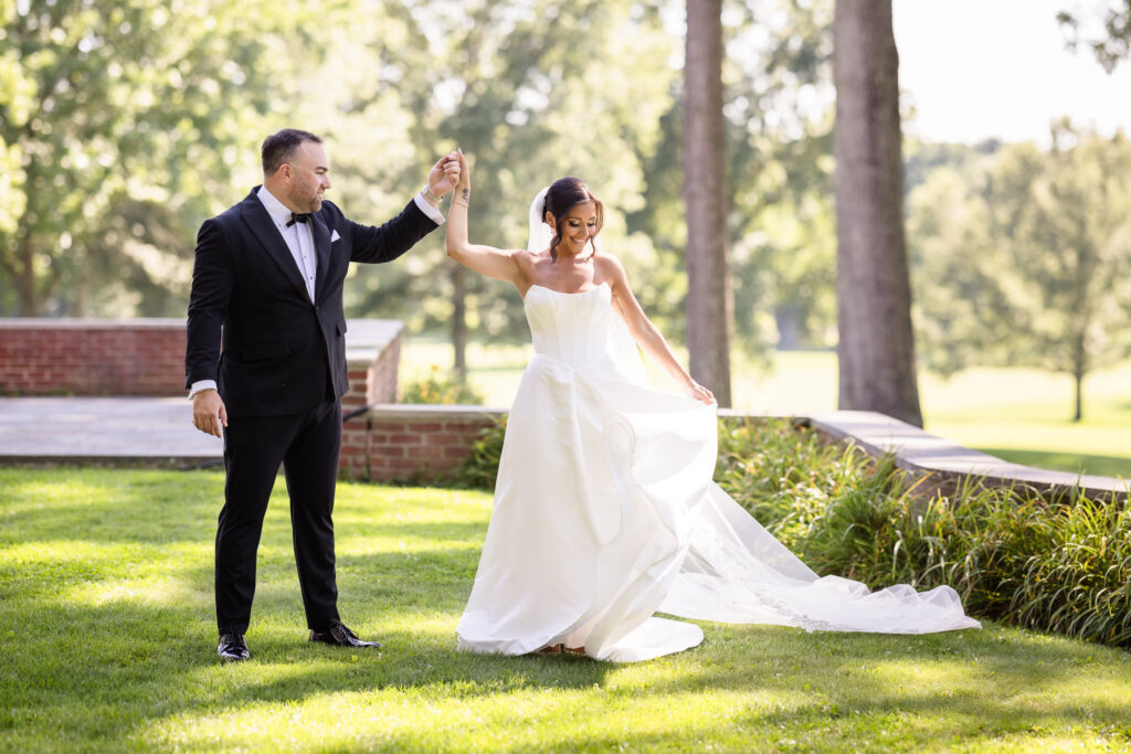 Bride and groom sharing a joyful moment together on the sunlit grounds of The Muttontown Club.