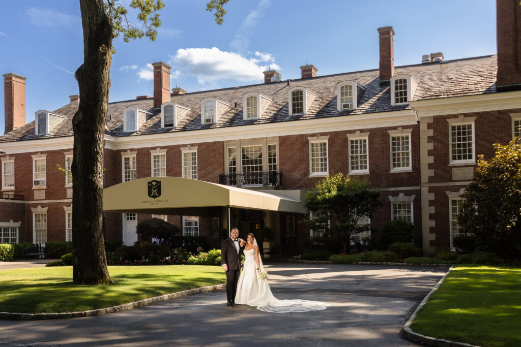 Bride and groom standing together in front of the historic exterior of The Muttontown Club.