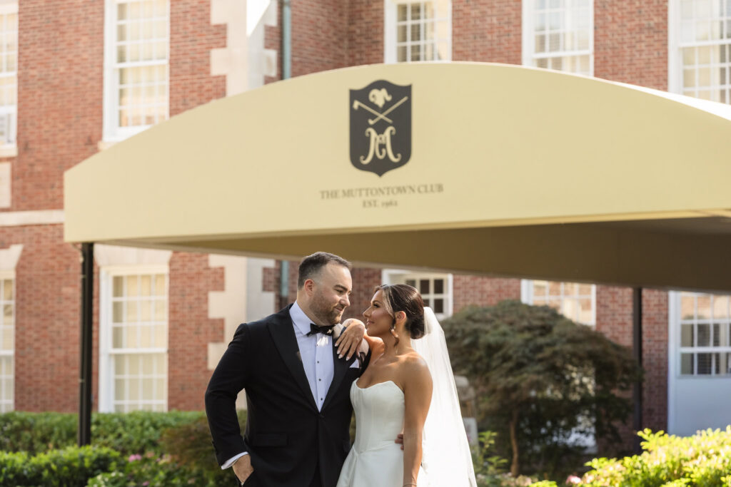 Bride and groom embracing beneath the entrance canopy at The Muttontown Club.