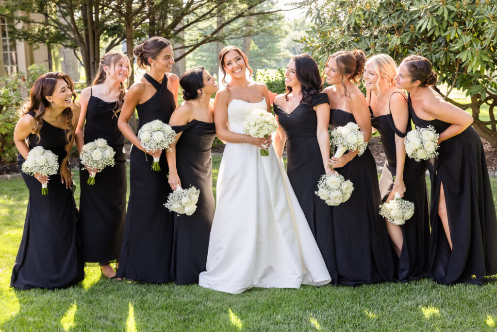Bride surrounded by her bridesmaids in black dresses during an outdoor wedding portrait at The Muttontown Club.