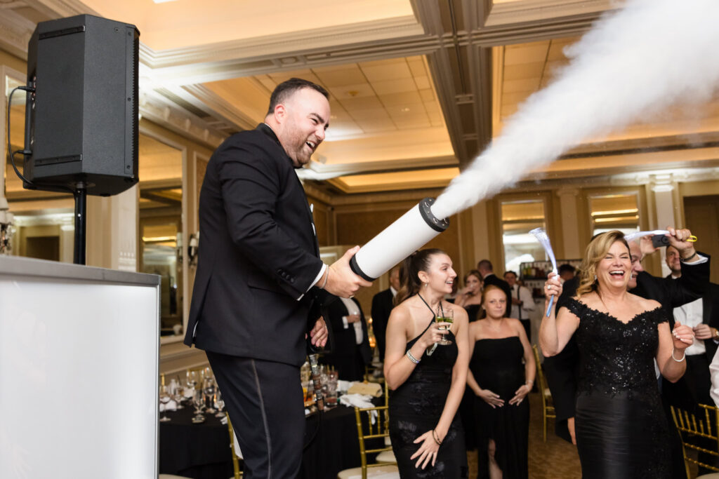 Groom laughing while using a CO2 cannon during the lively wedding reception celebration.