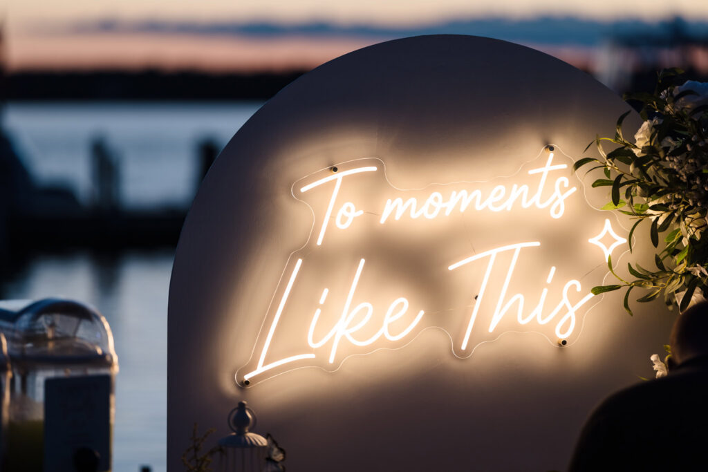 Glowing “To moments like this” sign overlooking the water.
