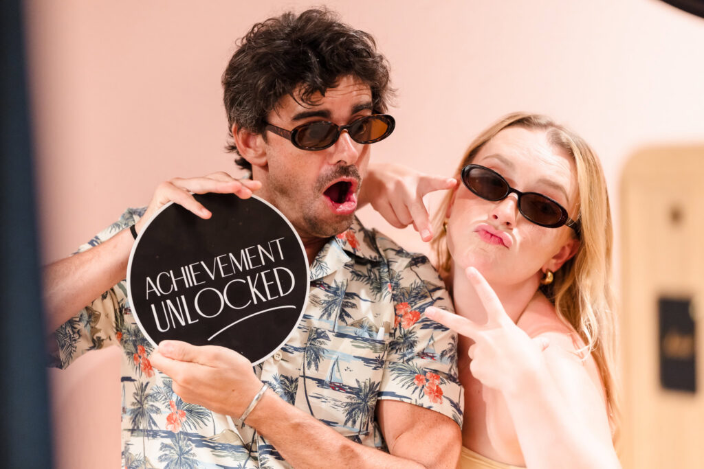 Two guests posing playfully with an “Achievement Unlocked” sign.