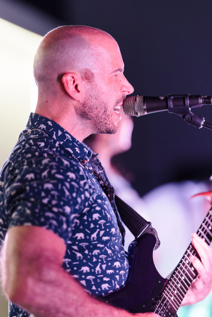 Guitarist singing into a microphone during a live performance in East Hampton.