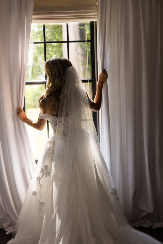 Kaity standing beside a window in her wedding gown and veil during preparations at the Rose Cottage on July 4th.