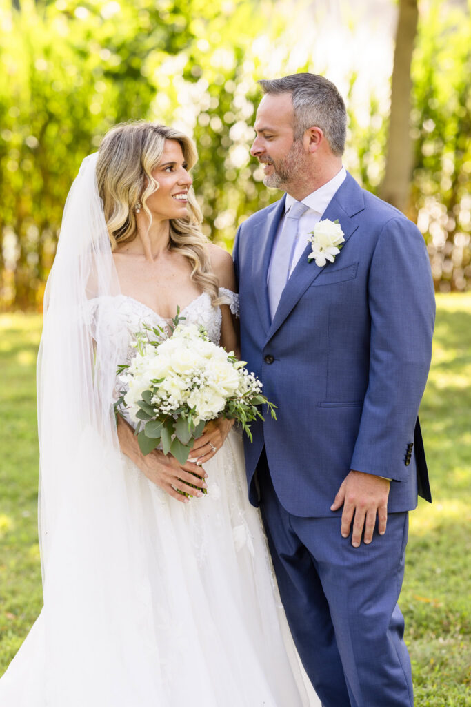 Kaity and Sean smiling at each other during wedding portraits in the gardens at Flowerfield.
