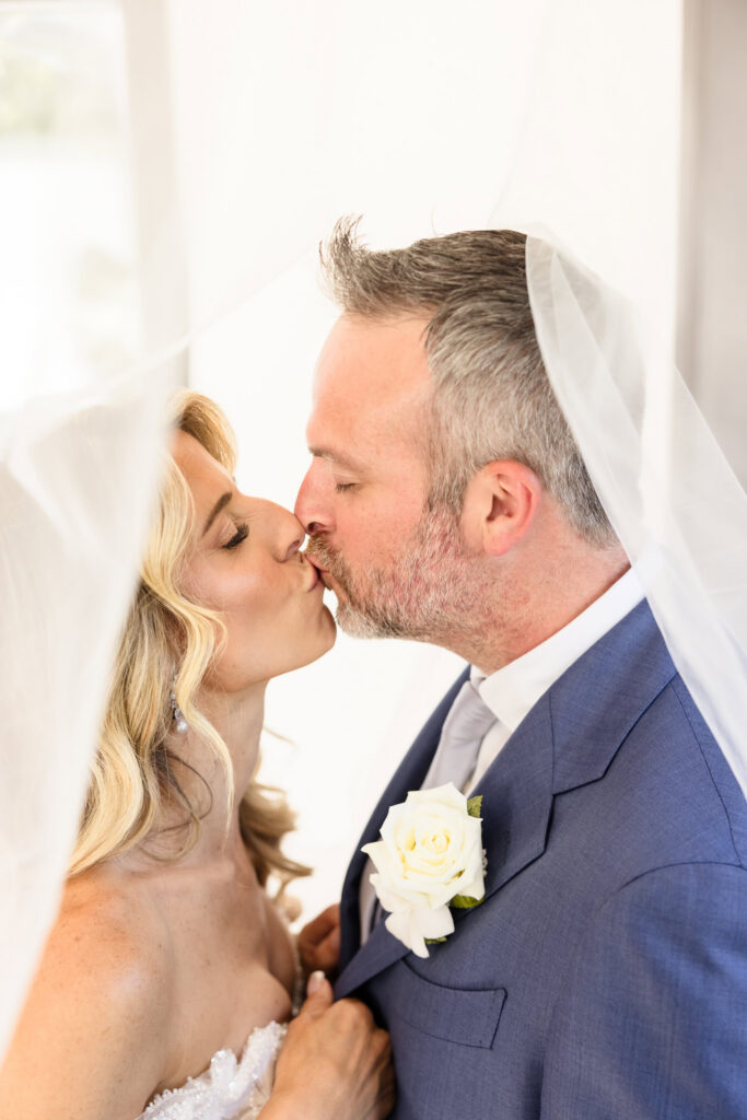 Kaity and Sean sharing a kiss beneath her wedding veil during portraits at Flowerfield on July 4th.