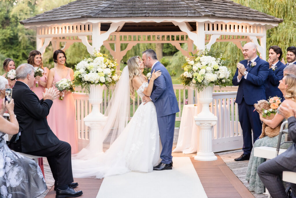 Kaity and Sean sharing their first kiss beneath the gazebo during their outdoor ceremony at Flowerfield.