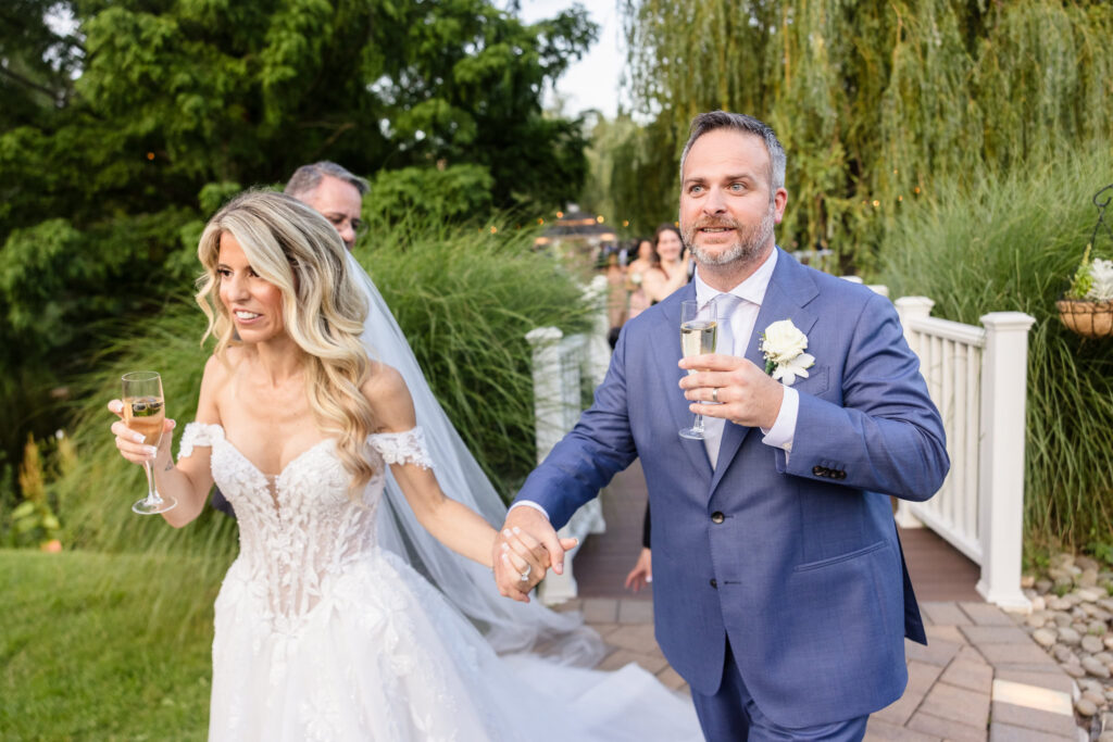 Kaity and Sean holding hands and carrying champagne after their outdoor summer wedding ceremony at Flowerfield.