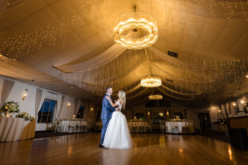 Kaity and Sean sharing their first dance beneath draped fabric and warm string lights at their Flowerfield reception.