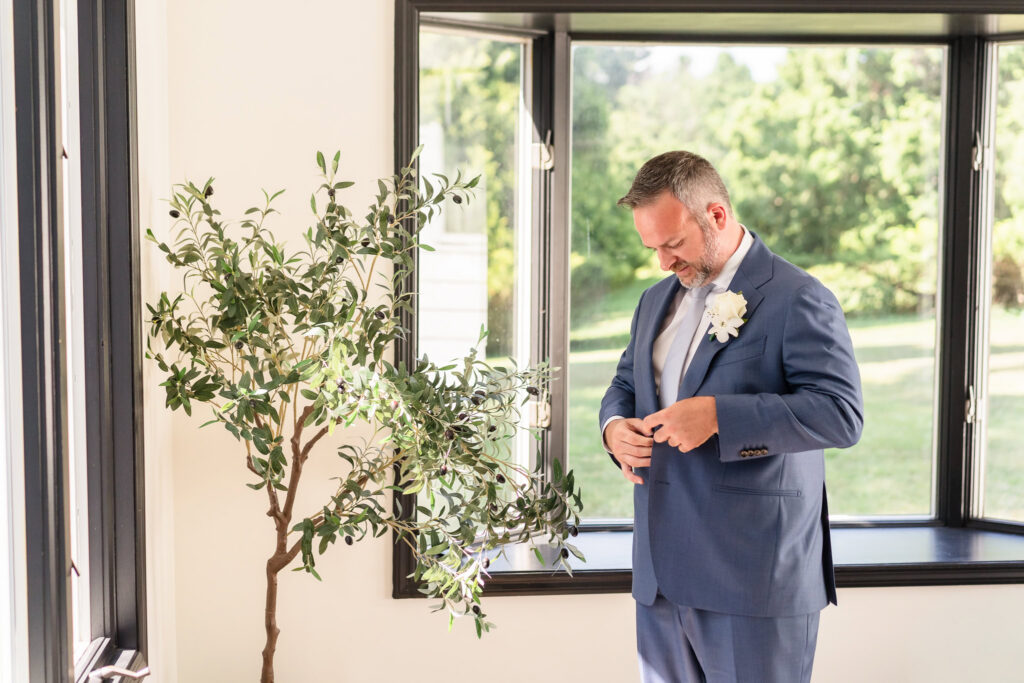 Sean buttoning his blue wedding suit while getting ready at Flowerfield in St. James.