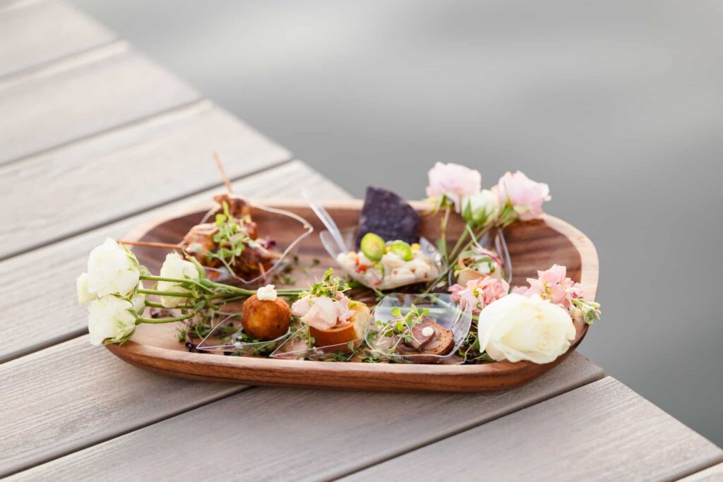 Assorted cocktail-hour bites and flowers arranged on a wooden tray at EHP Resort in East Hampton.