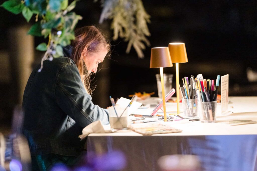 Live artist works beneath table lamps during hamptonBRIDE’s A Toast to Summer event in East Hampton.