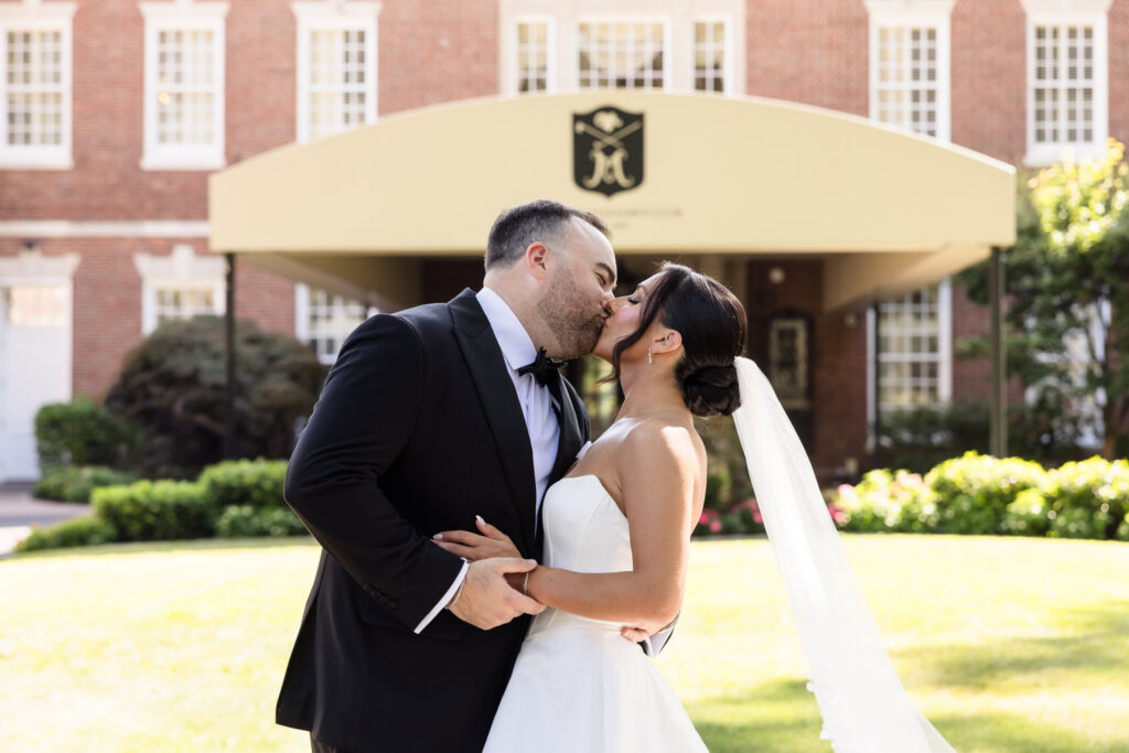 Christine and Matt kiss in front of the clubhouse during their summer wedding at The Muttontown Club.