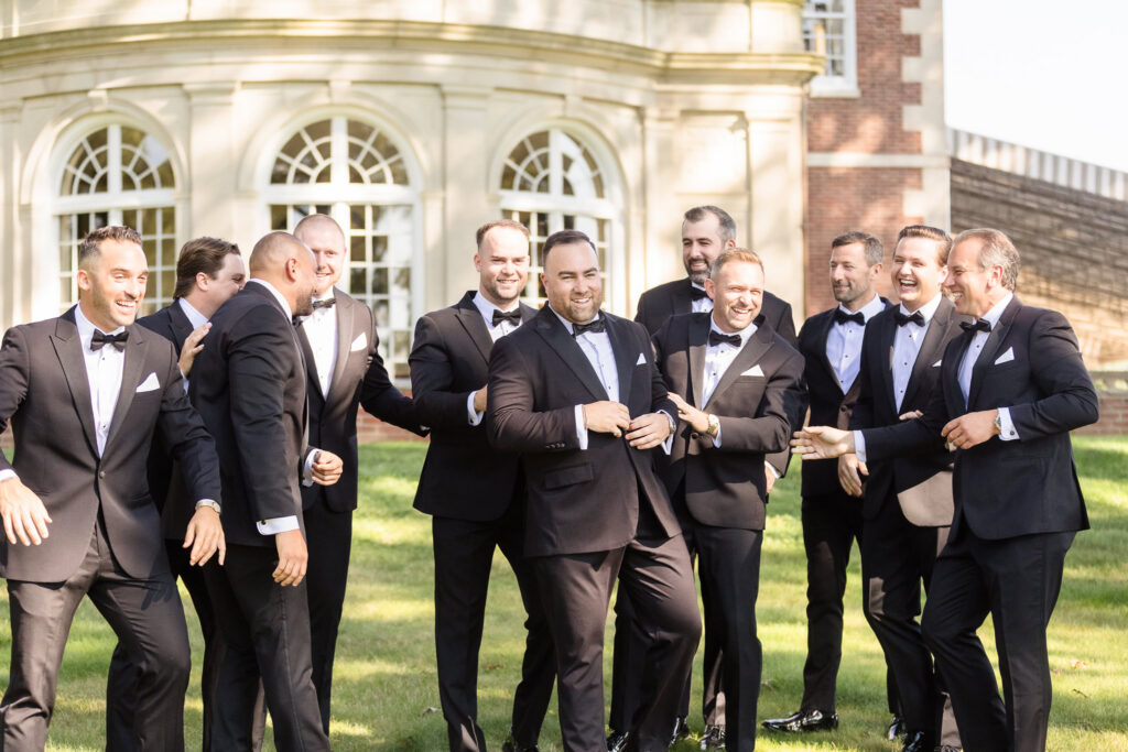 Matt laughs with his groomsmen in black tuxedos during wedding party portraits.