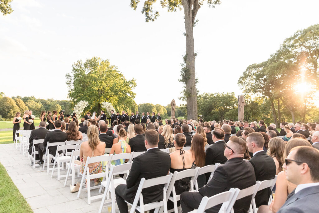 Wedding guests seated outdoors during a late-afternoon ceremony on the grounds of The Muttontown Club.