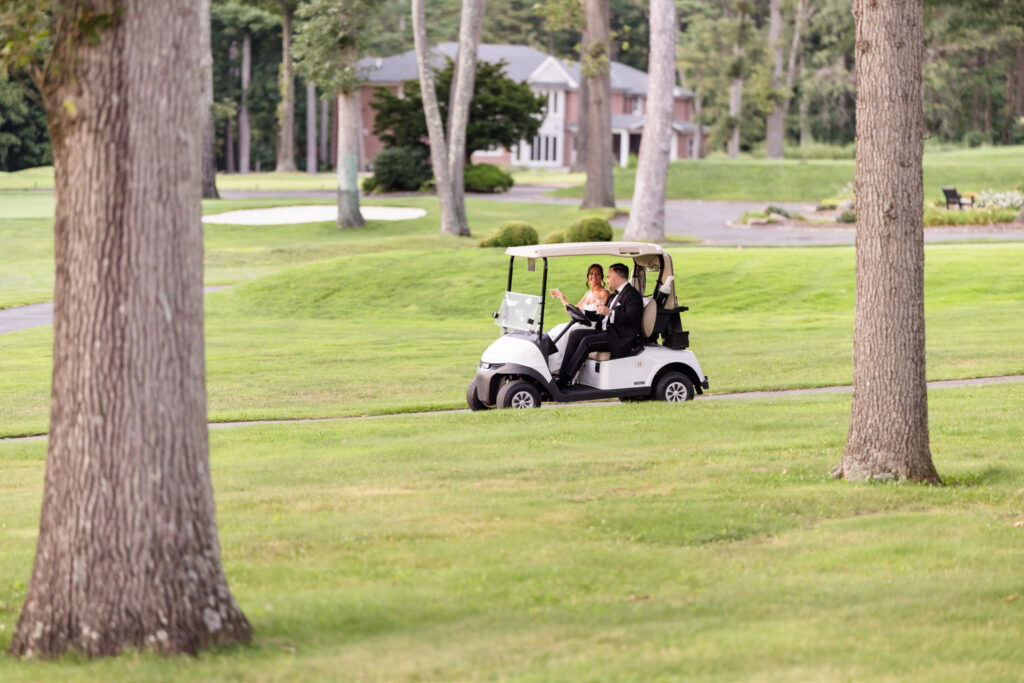 Newlyweds riding a golf cart across The Muttontown Club grounds during their wedding day.